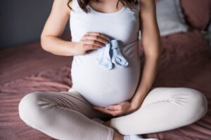 cómo hacer un bebé, mujer embarazada con unos patucos azules