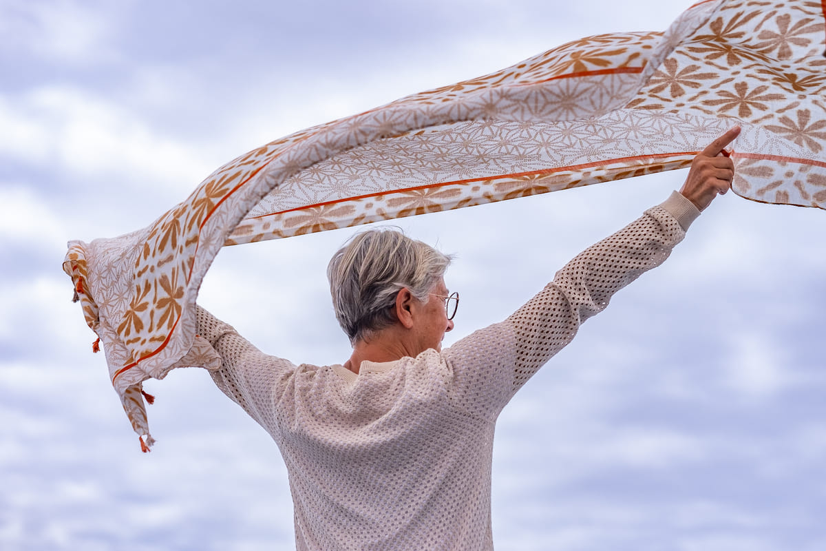 una mujer disfrutando de su envejecimiento activo y saludable lanzando un pañuelo al aire