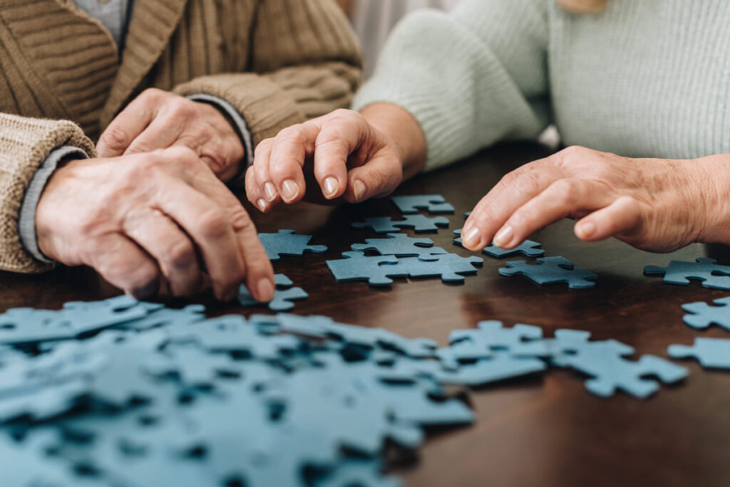 manos de personas mayores jugando a un puzle en un programa de estimulación cognitiva para personas mayores